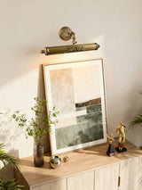 Scrolled brass bar lit over a framed canvas beside a small gold statue