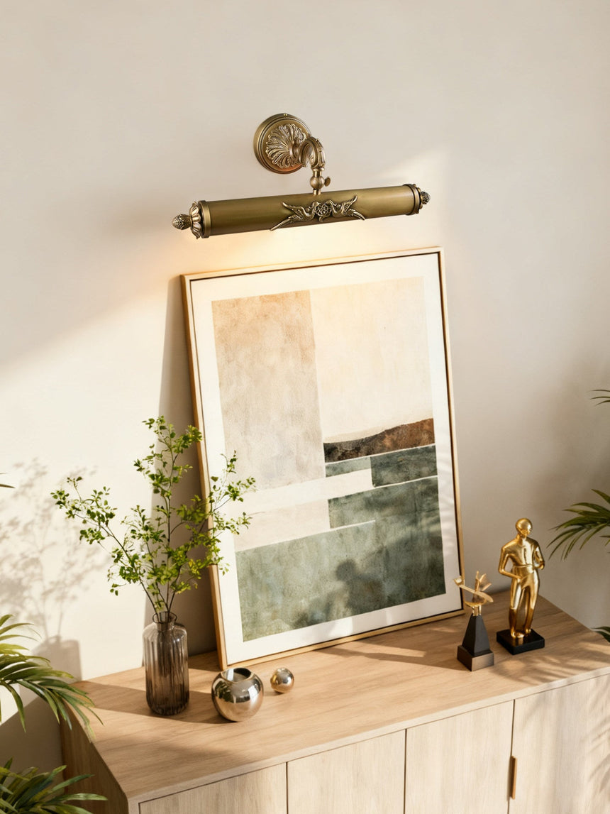 Scrolled brass bar lit over a framed canvas beside a small gold statue