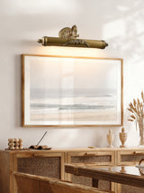 Scrolled brass bar lit over a framed seascape above a cane fronted console