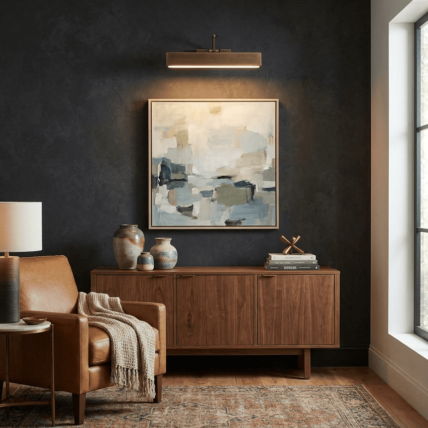 Bronze bar lit over a framed canvas on a dark wall above a walnut sideboard