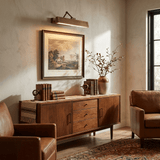 Bronze bar lit over a framed landscape above a walnut sideboard and a leather chair