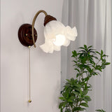 Sconce lit beside a curtain and a tall plant on a pale plaster wall
