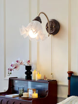 Sconce lit above a dark dresser with candles and orchids beside a bed