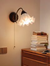 Sconce lit above a wood chest holding a tall stack of worn books