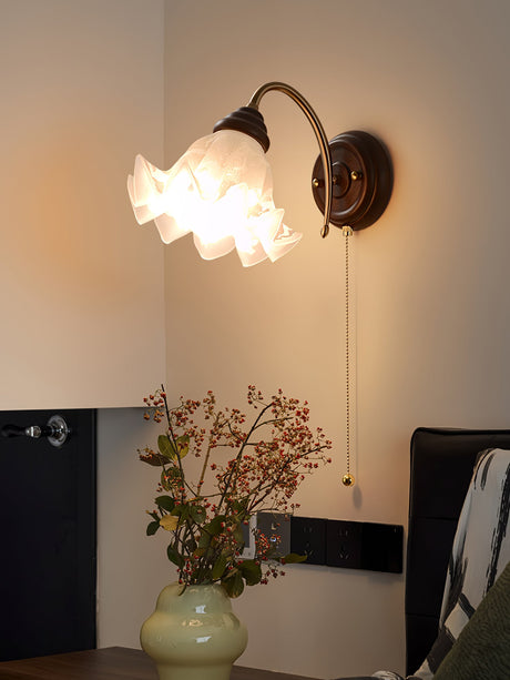 Sconce lit above a green vase of branches beside a dark wood cabinet