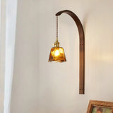 Amber glass shade lit warm on the wood arm beside a curtain and a frame