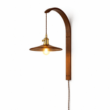 Dark amber cone shade lit from within on the curved wood hook arm