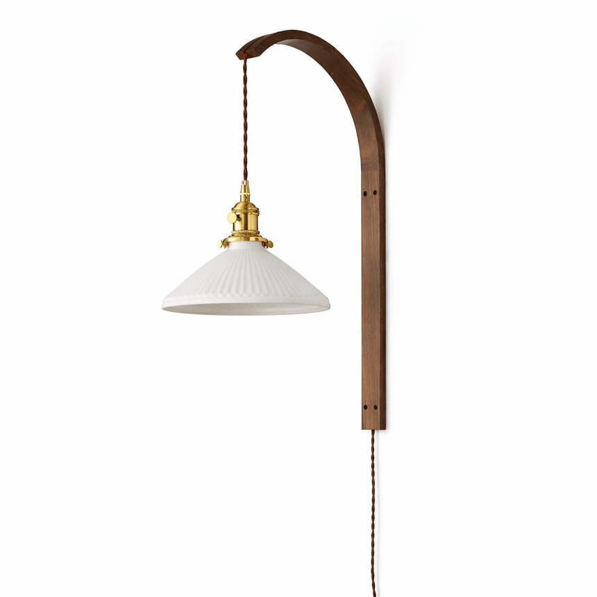 Ribbed white glass cone shade lit warm on the curved wood hook arm