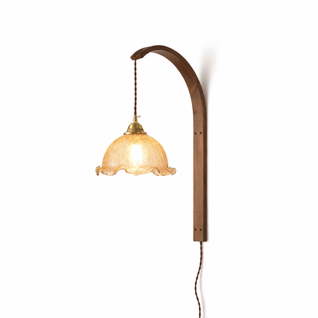 White scalloped glass shade lit warm, the brass socket and cord above it
