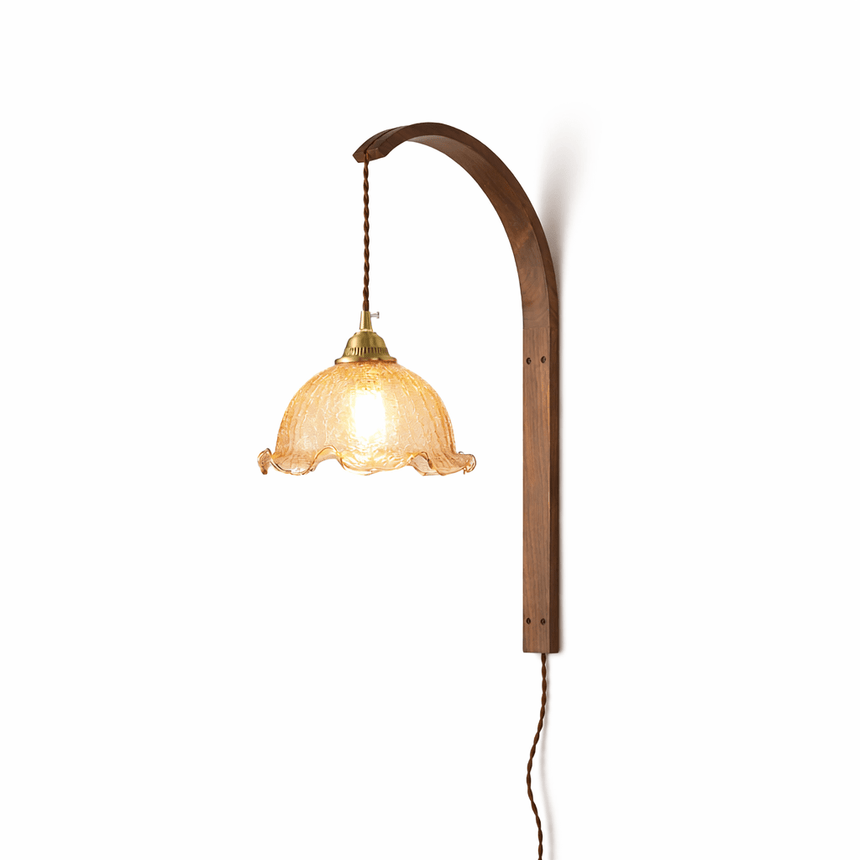 White scalloped glass shade lit warm, the brass socket and cord above it