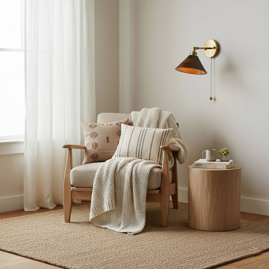 Sconce lit beside a curtained window above a cane armchair