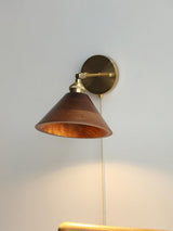 Walnut cone sconce lit and seen at an angle on a plain wall
