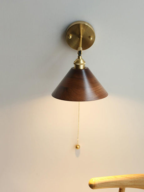 Walnut cone sconce unlit on a plain wall with the pull cord hanging