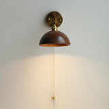Rounded walnut dome sconce unlit, the brass pull cord hanging below