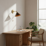Walnut sconce lit above a wood desk with a plant and a chair