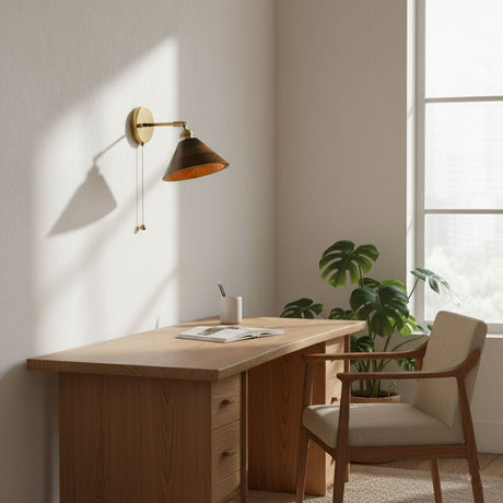 Walnut sconce lit above a wood desk with a plant and a chair