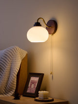 Rounded white glass shade lit and angled down beside a bed
