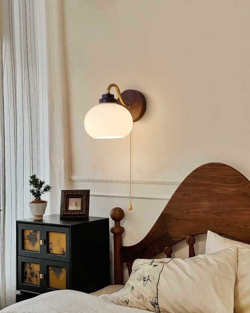 Rounded glass shade lit above a wood headboard beside a cabinet