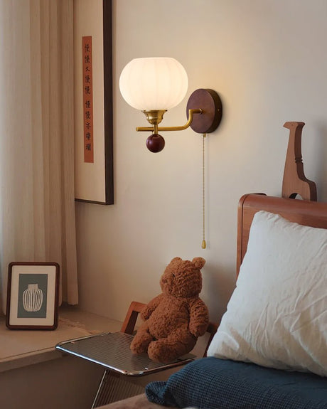 Ribbed glass sconce lit in a bedroom beside a scroll and a pillow