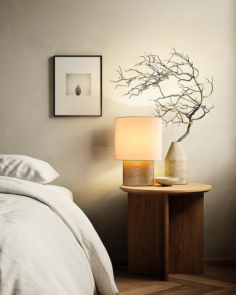 Wabi sabi table lamp lit beside a bed with dried branches