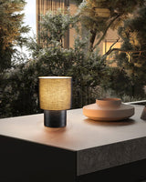 Wabi sabi table lamp on a dark table beside a window and greenery