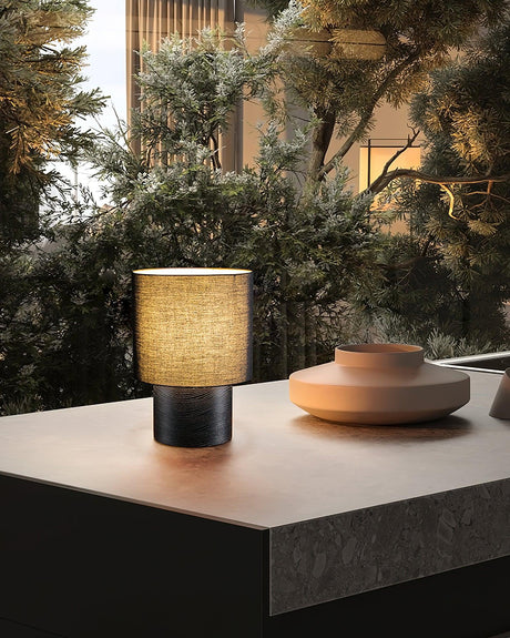 Wabi sabi table lamp on a dark table beside a window and greenery