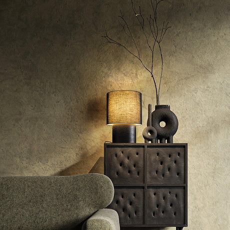 Wabi sabi table lamp lit on a carved wood cabinet in a dim room