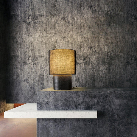 Wabi sabi table lamp lit on a pale ledge against a dark wall