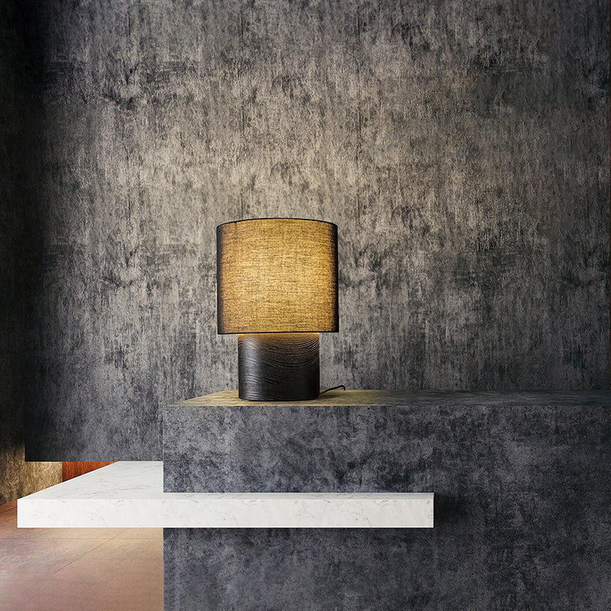 Wabi sabi table lamp lit on a pale ledge against a dark wall