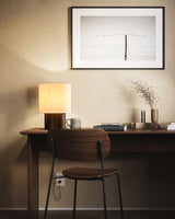 Wabi sabi table lamp lit on a slim desk below a framed print