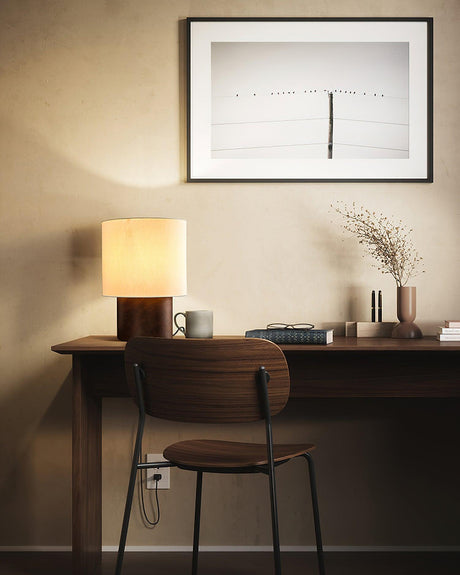 Wabi sabi table lamp lit on a slim desk below a framed print