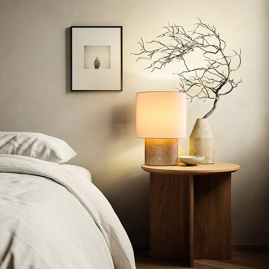 Wabi sabi table lamp lit on a round nightstand beside a made bed