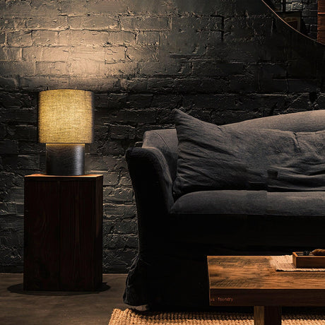 Wabi sabi table lamp lit on a wood block beside a dark sofa