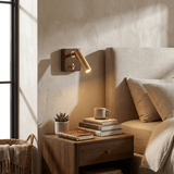 Reading lamp lit above a nightstand with books and a small cup