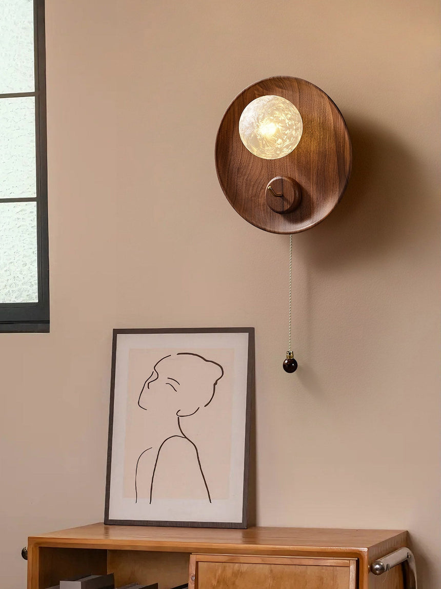 Sconce lit above a wood console with a framed line drawing and a window