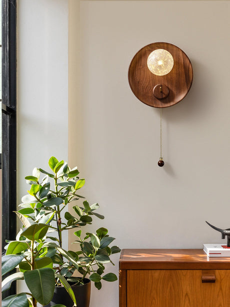 Sconce lit beside a plant above a wood desk holding a stack of books