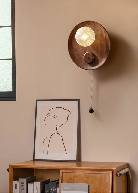 Sconce lit above a wood sideboard with framed artwork, books and a window