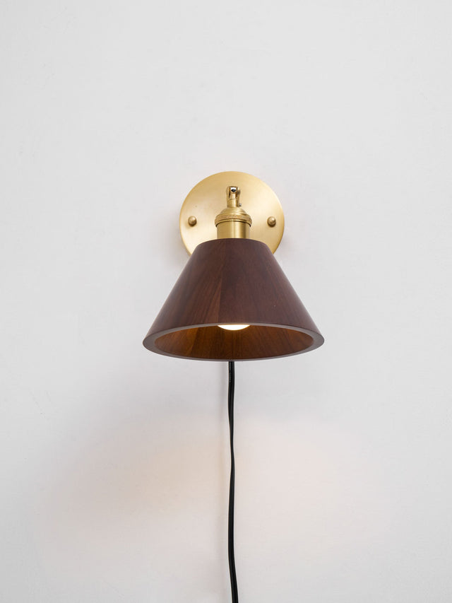 Walnut cone shade on a brass arm with the cord running down the wall