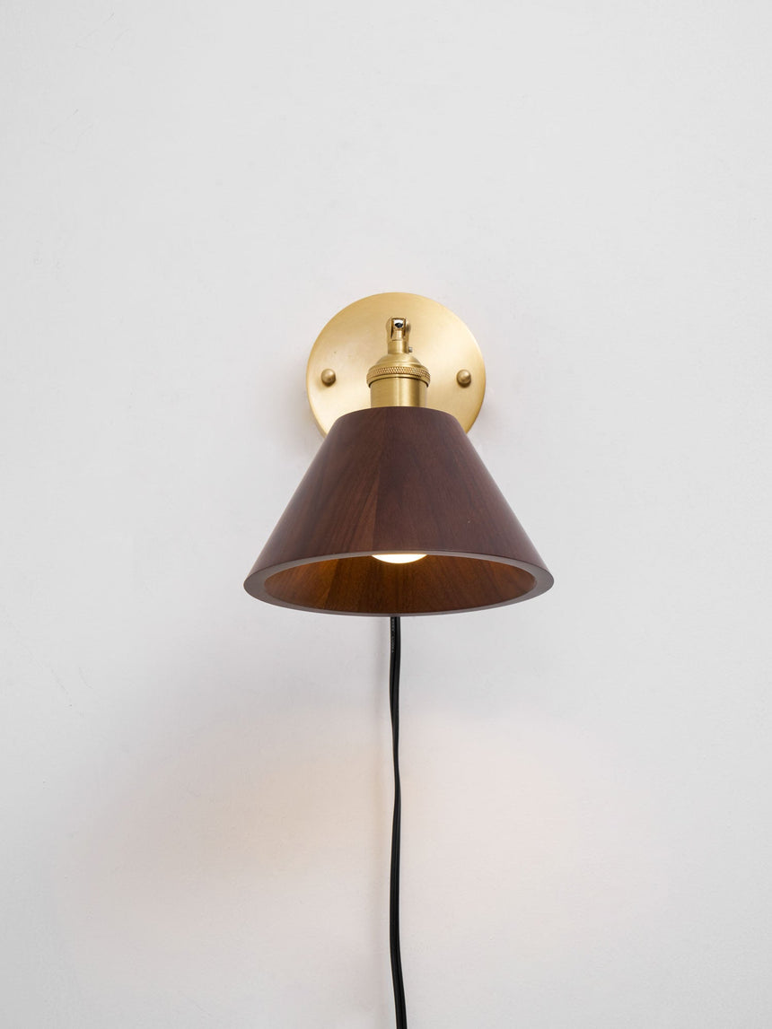 Walnut cone shade on a brass arm with the cord running down the wall