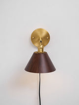 Walnut cone sconce unlit on a pale wall, cord hanging from the plate