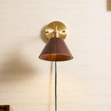 Walnut cone sconce lit on a pale wall above a wood cabinet