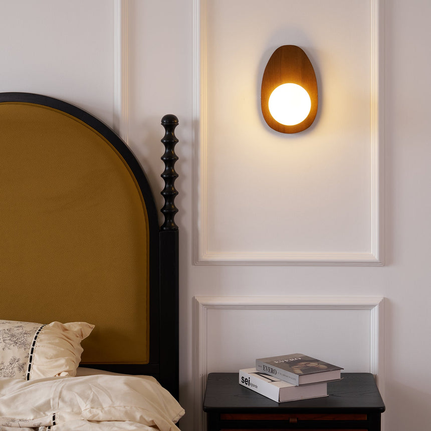 Walnut oval sconce lit beside a bed with a mustard headboard