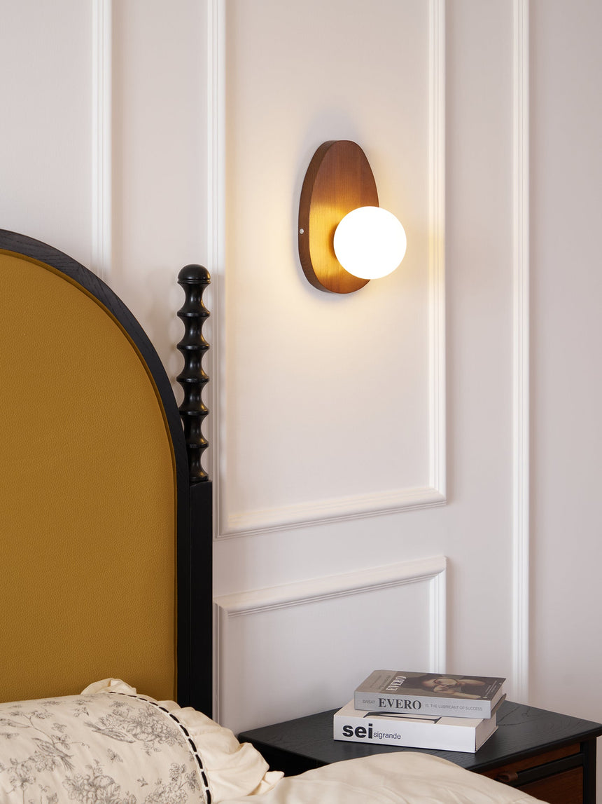 The sconce lit above a nightstand beside a made bed at night