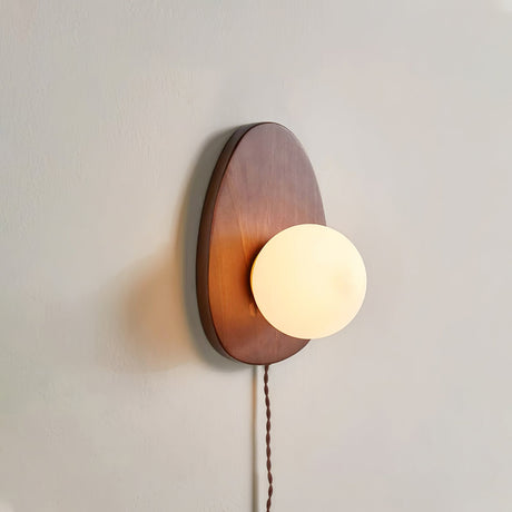 Side view of the walnut plate and the sphere against a plain wall