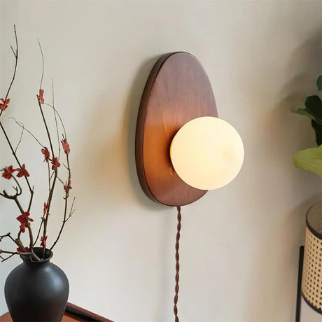 Walnut oval sconce beside a vase of branches on a dark cabinet