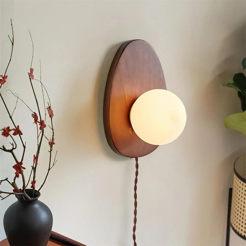 Walnut oval sconce beside a vase of branches on a dark cabinet