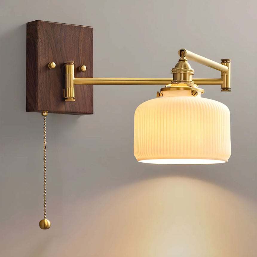 Ribbed white ceramic drum shade lit, brass arm folded against the wall