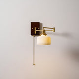 White ceramic shade unlit on a brass arm, seen against a pale wall