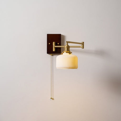 White ceramic shade unlit on a brass arm, seen against a pale wall