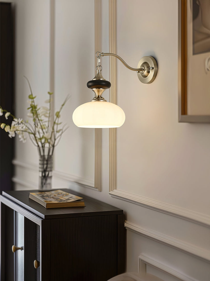Lamp lit in a hallway above a dark cabinet holding a vase of branches